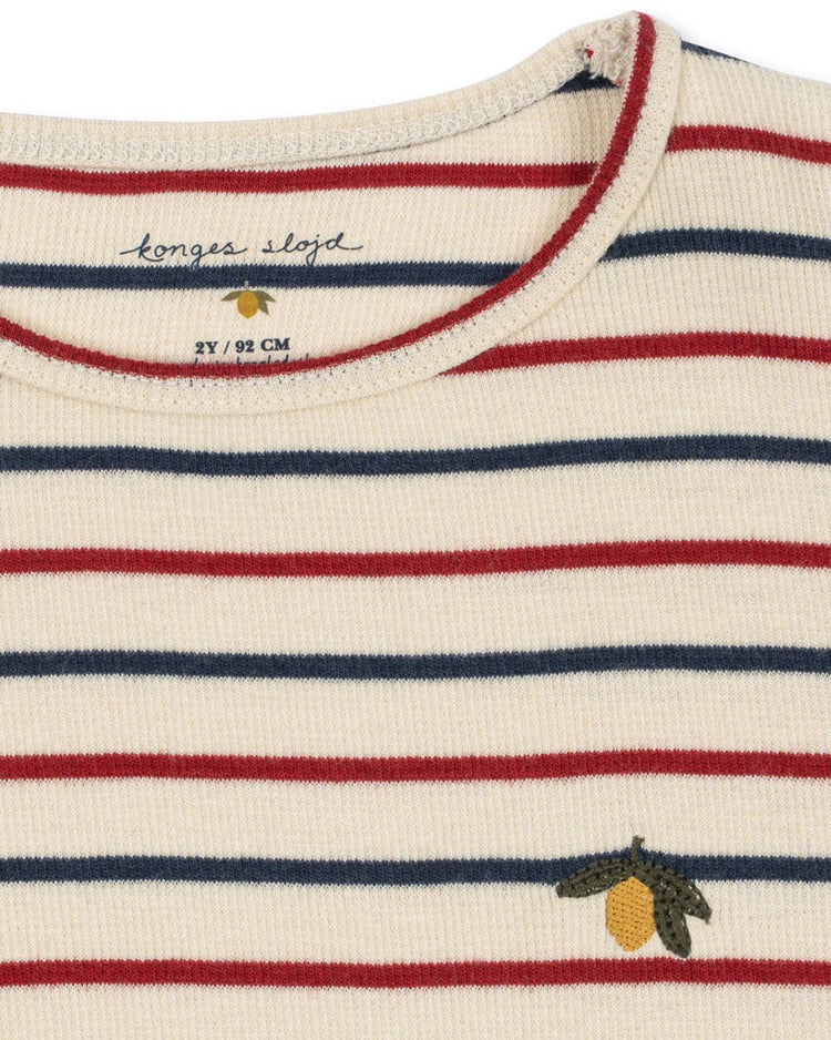 Cream-colored voco modal blouse in tricolore bleu by konges sløjd, featuring horizontal red and navy stripes crafted from structured rib for added texture and durability. Adorned with a small embroidered yellow fruit with green leaves near the hem and finished with an interior konges sløjd label at the collar.