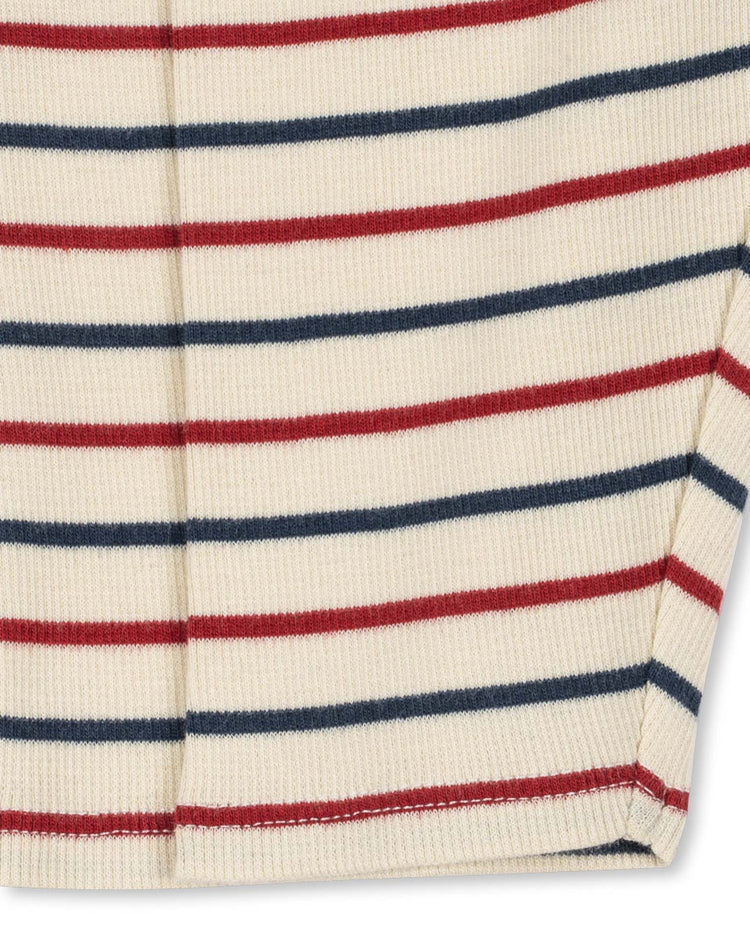 Close-up of a ribbed cream fabric featuring horizontal red and navy blue stripes, showing part of the garment with a seam and a small slit at the hem—crafted from an organic cotton-modal blend for enhanced breathability and comfort. Shown: konges sløjd voco modal pants in tricolore bleu.