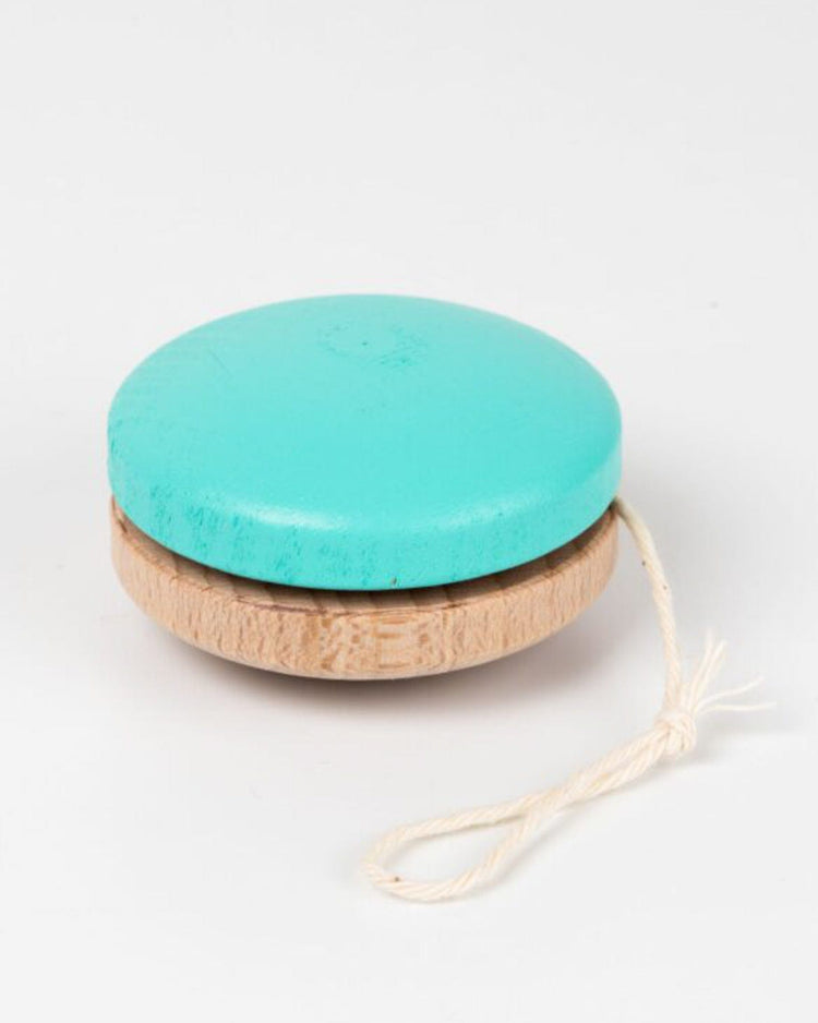 A turquoise wooden yo yo from me & mine, painted with eco-friendly colors and featuring a white string, is displayed on a plain white background.
