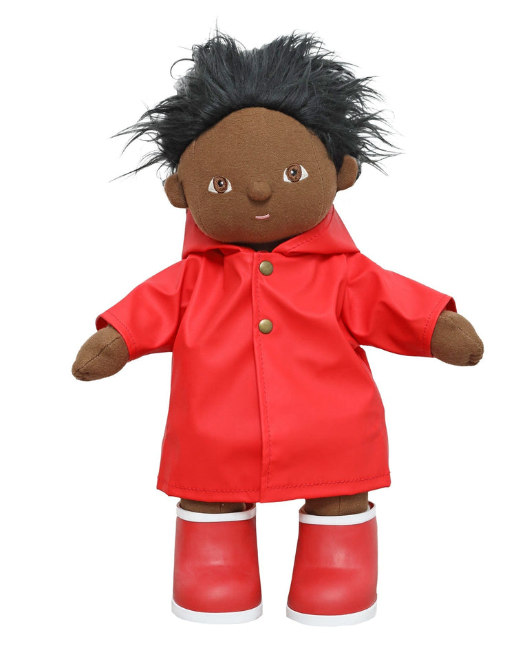 A soft, brown-skinned dinkum dolls doll with spiky black hair wears the 14-inch dinkum doll ahoy raincoat in red and matching boots, standing against a white background.