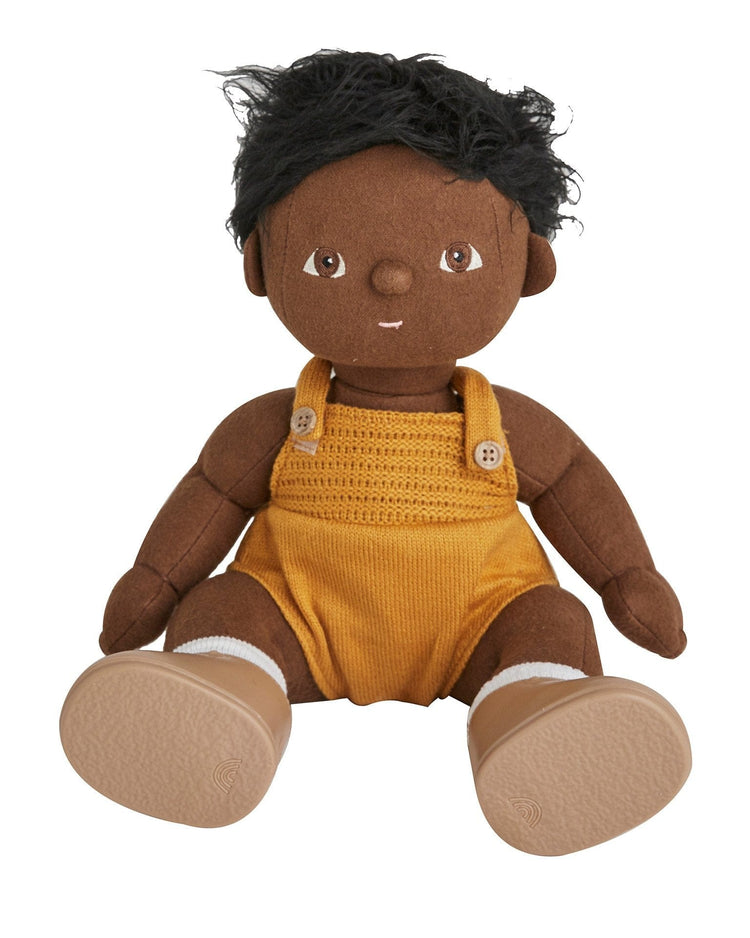 A plush dinkum doll - tiny from dinkum dolls features dark brown skin, black yarn hair, large embroidered eyes, yellow overalls with two buttons, and tan shoes. This posable doll brings comfort and charm to playtime.