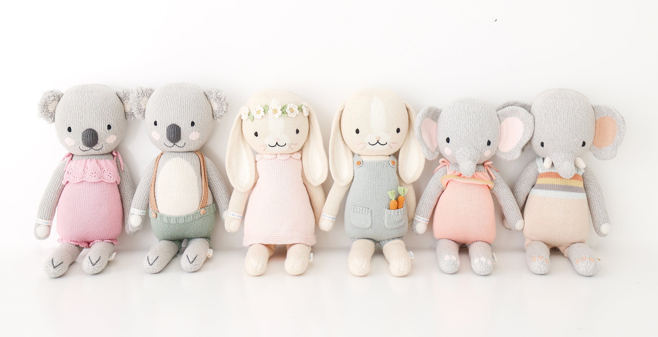 Six stuffed animal toys are lined up side by side against a white background. They include two koalas, two rabbits, and two elephants, all dressed in pastel colored clothing.