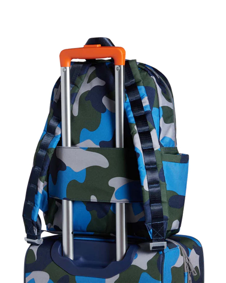 A kane backpack in camo from state bags is shown secured to the handle of a suitcase, illustrating how it conveniently fits over rolling luggage for easy transport.