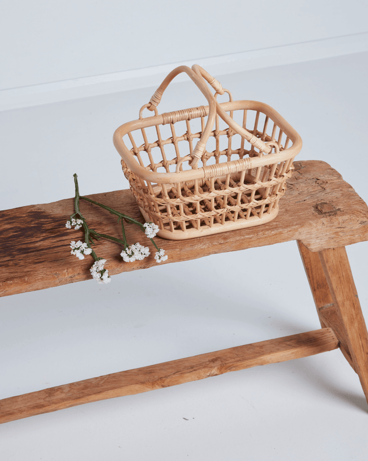 A tarry basket in wheat by dinkum dolls with two handles sits on a rustic wooden bench next to white flowers, against a plain white background—perfect as a charming kids storage basket.