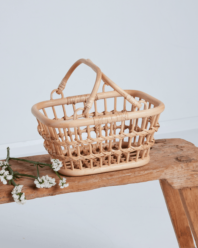 A small, rectangular dinkum dolls tarry basket in wheat with two handles sits on a rustic bench beside white flowers, against a plain background—perfect as a charming kids storage basket.