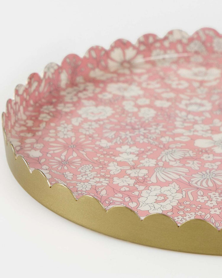 The meri meri x Liberty round medium accessory tray by meri meri features a scalloped gold edge and a pink floral pattern with white and light pink flowers and leaves.