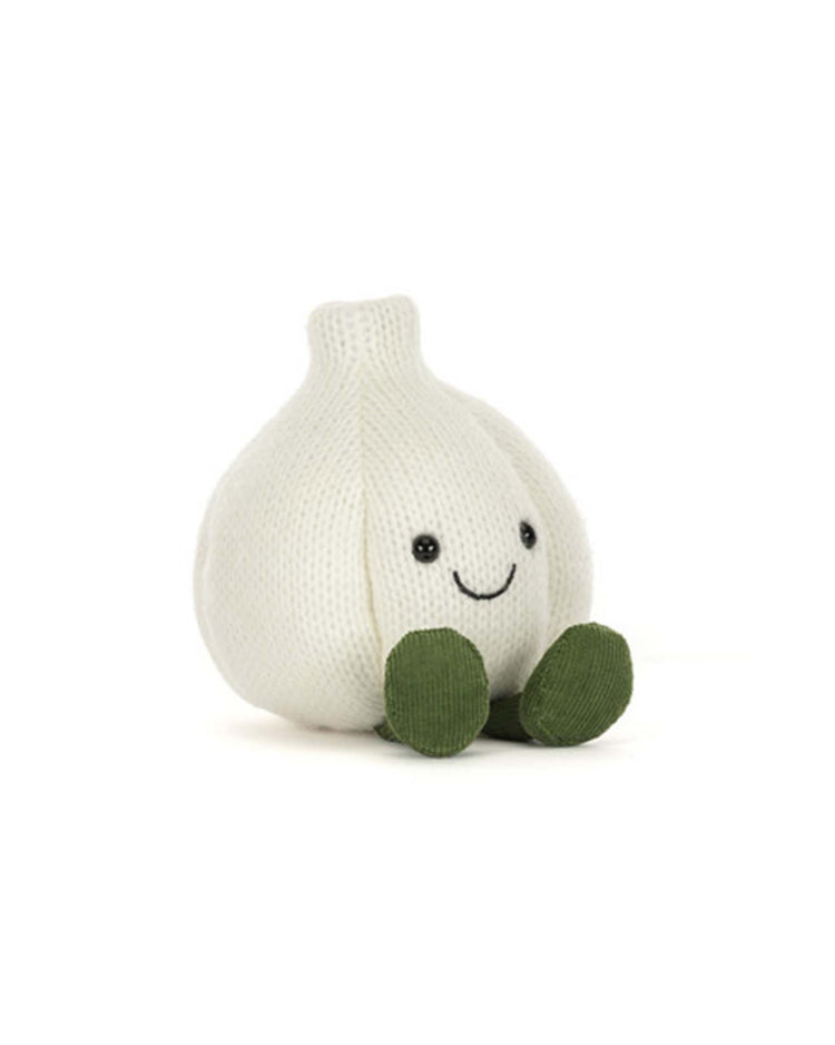A plush toy shaped like a garlic bulb with a smiling face, black eyes, and green feet sits on a white background—this adorable Jellycat Amuseables Garlic is the perfect companion for a Halloween party or to bring some quirky charm to your home.