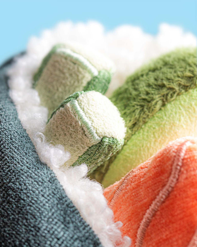 Close-up of a Jellycat Amuseables Coneroi Temaki plush, designed to look like sushi with soft pieces resembling cucumber, avocado, and salmon—ideal for party planners or event coordinators—set against a light blue background.
