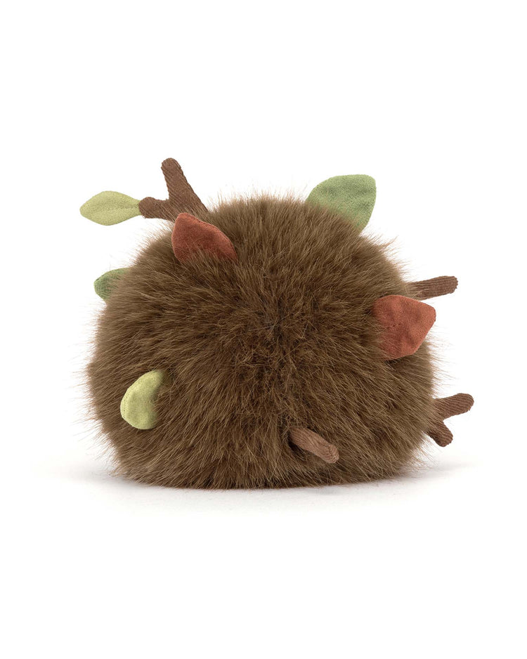 The amuseables mulshi woodland floor by jellycat is a round, fluffy brown plush toy with soft fabric branches and green or brown leaves, resembling a moss ball or bush, shown on a plain white background.