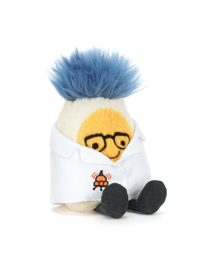 The amuseables boiled egg scientist outfit by jellycat is a plush toy with blue fluffy hair, round glasses, and a white shirt embroidered with a rocket. It has yellow and black facial features, black feet, and sits against a white background.