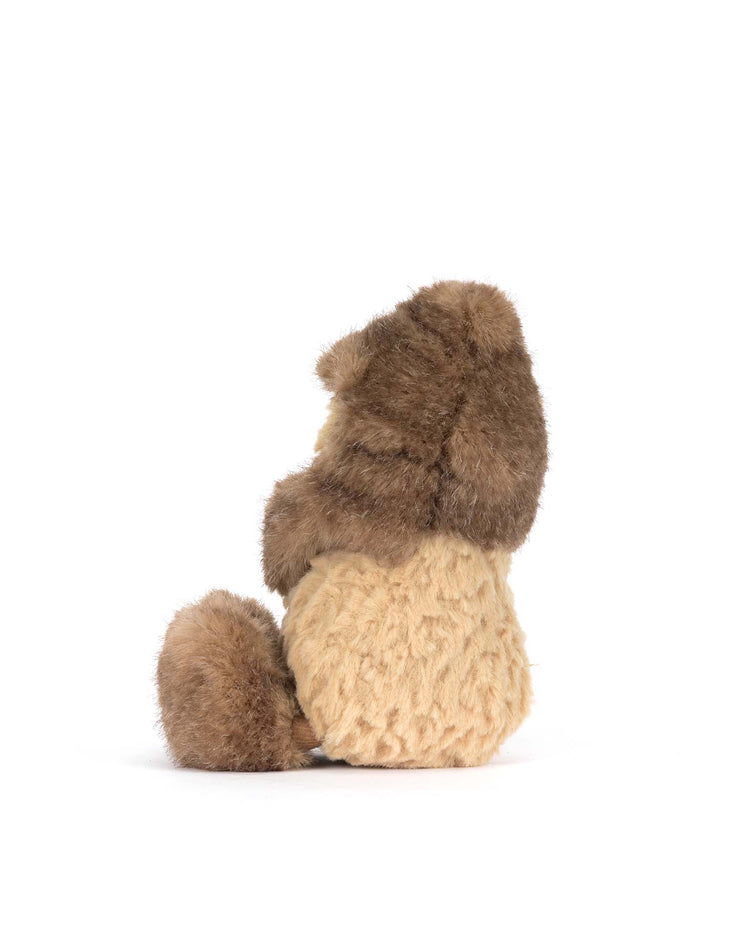 A plush stuffed animal from Jellycat, the Amuseables Peanut Yeti Outfit, sits upright with its back turned as if ready for a forest quest—perfect for fans. A plain white background highlights its adorable design.
