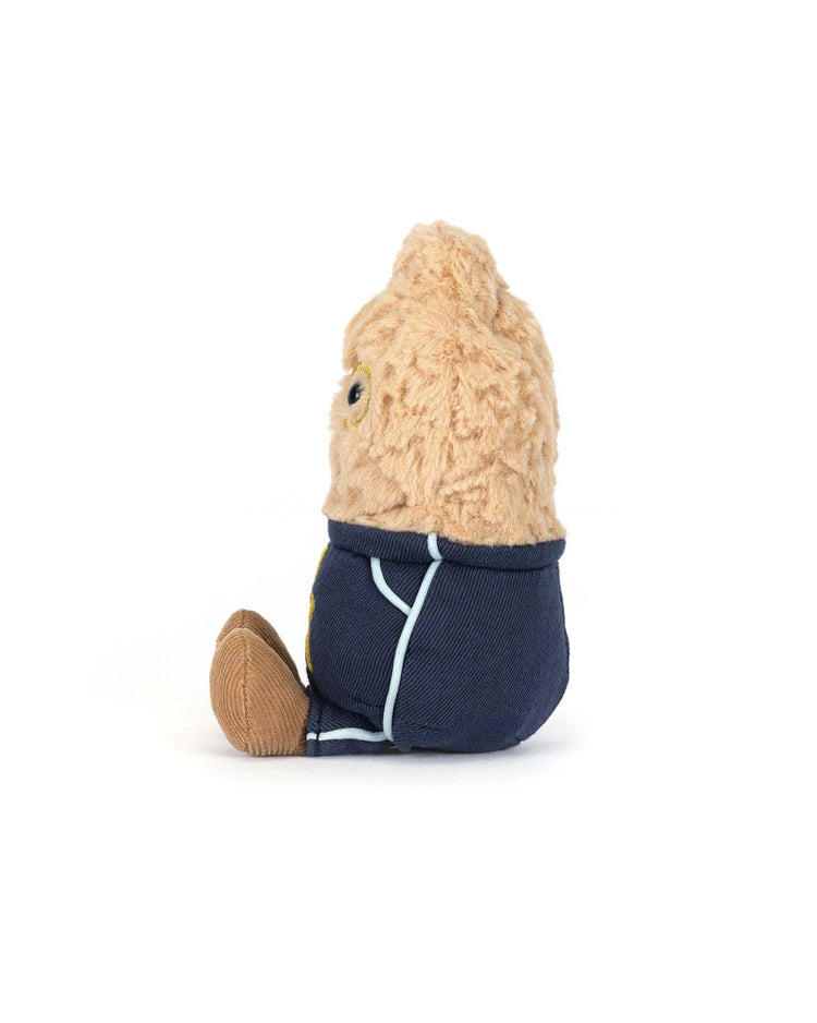 A side view of a small Jellycat amuseables peanut plush, dressed in a star student outfit, sitting upright on a white background.