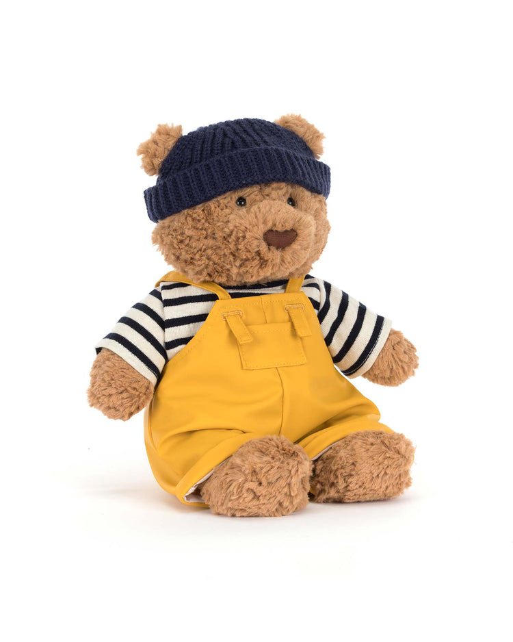 The Jellycat Bartholomew Bear Seafarer Outfit features a plush bear in yellow overalls, a navy knit beanie, and a black-and-white striped shirt—perfect for nautical adventures, shown against a plain white background.