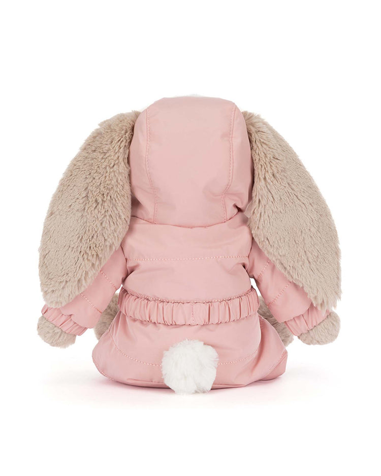 The jellycat bashful bunny 'snow suit' winter plush has long beige floppy ears and wears a pink hooded coat, shown from the back with a small white tail peeking out from beneath the coat.
