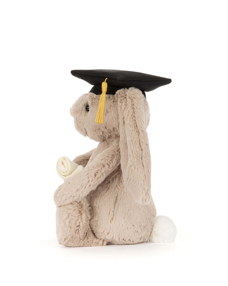 The jellycat bashful bunny graduation outfit features a plush bunny with a white tail, black graduation cap, yellow tassel, and rolled diploma—an ideal graduation gift.