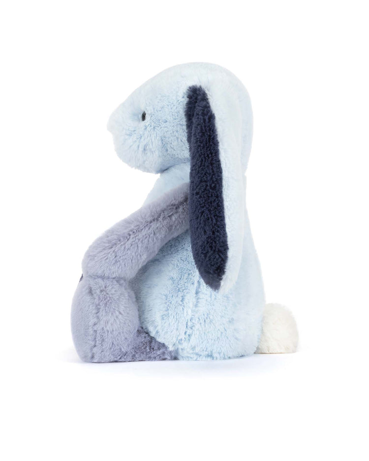 A Jellycat Puddlesea Bunny Original plush in light blue with dark blue inner ears, a white tail, and black stitched eyes sits upright in profile view against a white background.