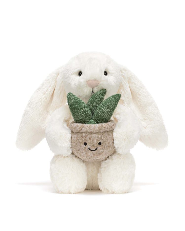 The jellycat cream bunny with plant features a plush bunny with long ears, sitting upright and holding a potted plant with green fabric leaves—a delightful gift. Shown against a plain white background.