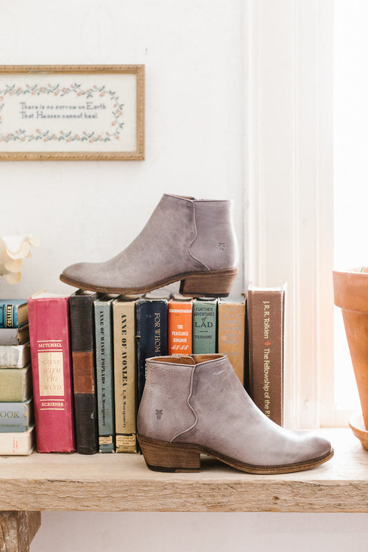 A pair of gray ankle boots displayed on a shelf beside a row of vintage books with a light background.