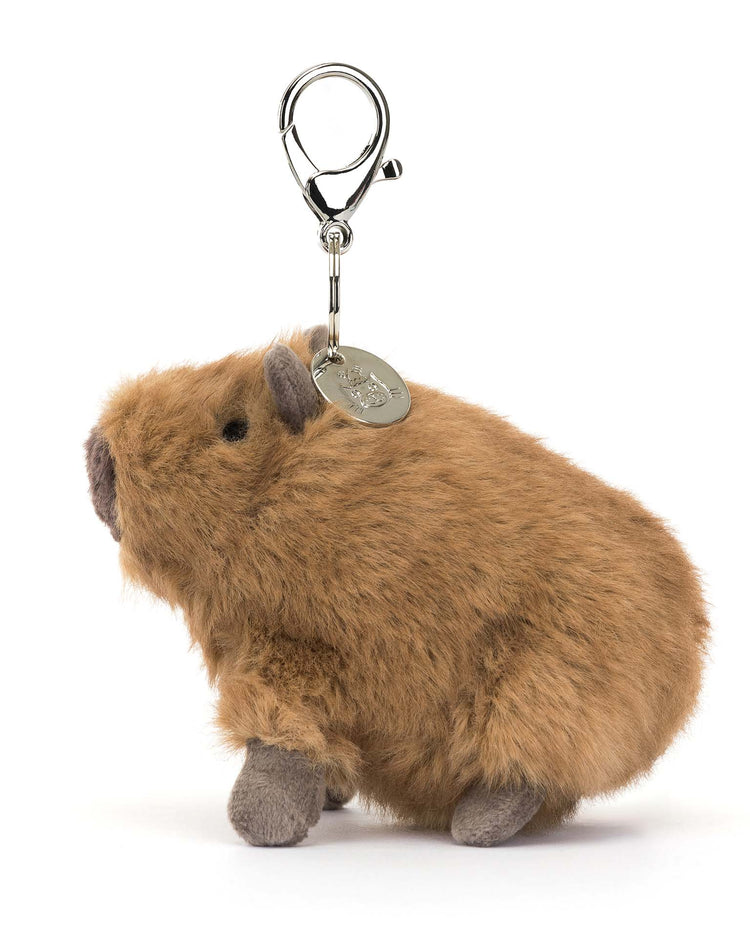 Discover the charming Clyde Capybara bag charm by Jellycat, featuring a fluffy brown design and a silver claw clip for easy attachment. Ideal for bags, it comes with a metal clasp and tag on a crisp white backdrop.