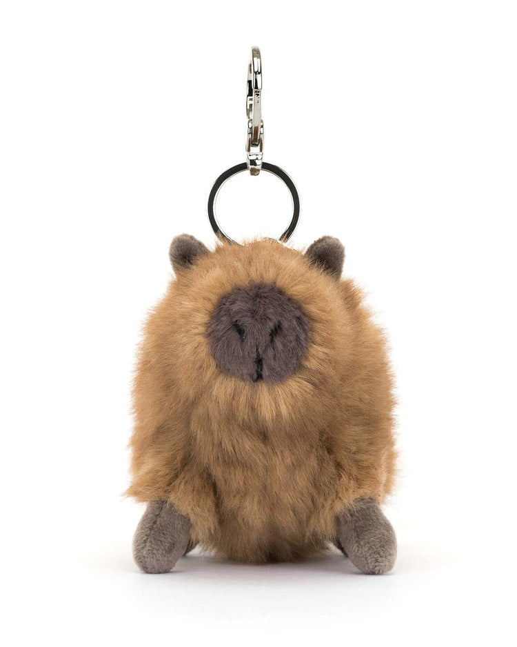 This plush keychain by Jellycat, called the Clyde Capybara Bag Charm, features fluffy brown fur and small ears. It has a sturdy metal key ring and a silver claw clip for easy attachment to your accessories, making it perfect as a bag charm.
