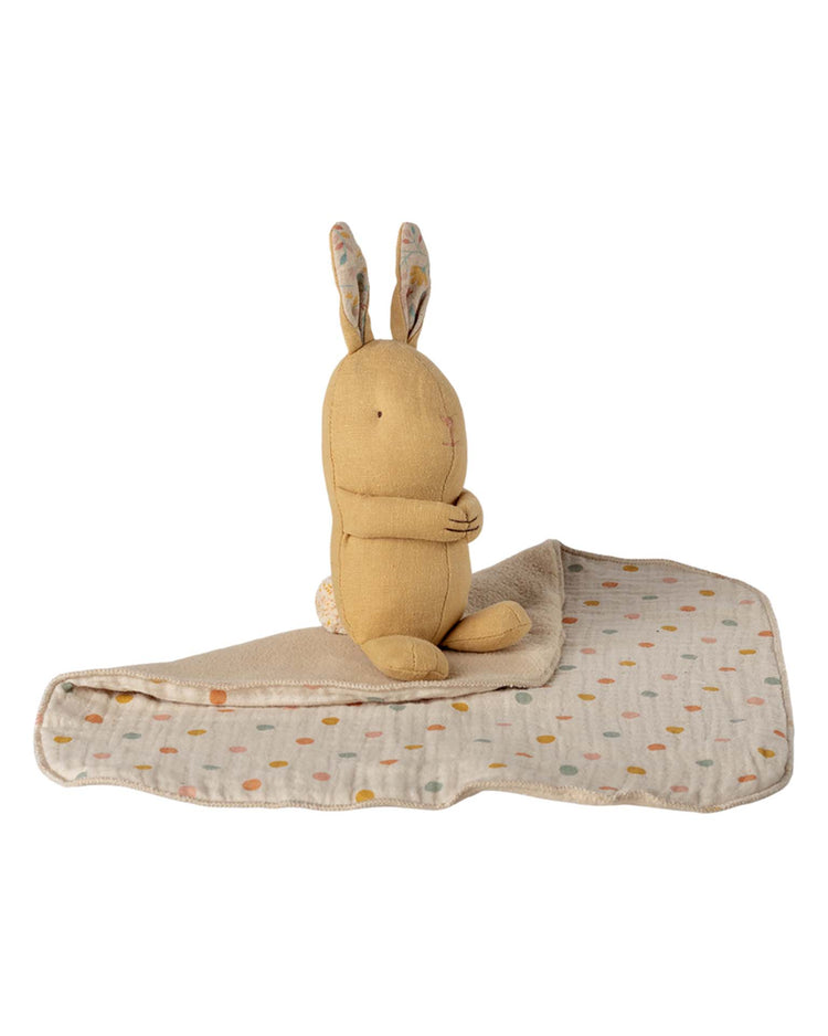 The maileg lullaby friends, bunny, mini in cream yellow sits with arms crossed on a beige blanket with colorful dots—a perfect newborn gift.