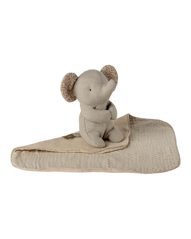 The maileg lullaby friends, elephant, mini - iron grey is a soft plush toy with patterned ears, sitting upright on a textured beige baby blanket—a charming newborn gift for snuggles and play.