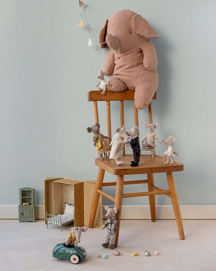 Maileg’s wedding mice couple in box, mum and dad, dressed in charming outfits, are displayed with cute toy props and small furniture beside a wooden chair, while a large stuffed elephant sits on top against a light blue wall.