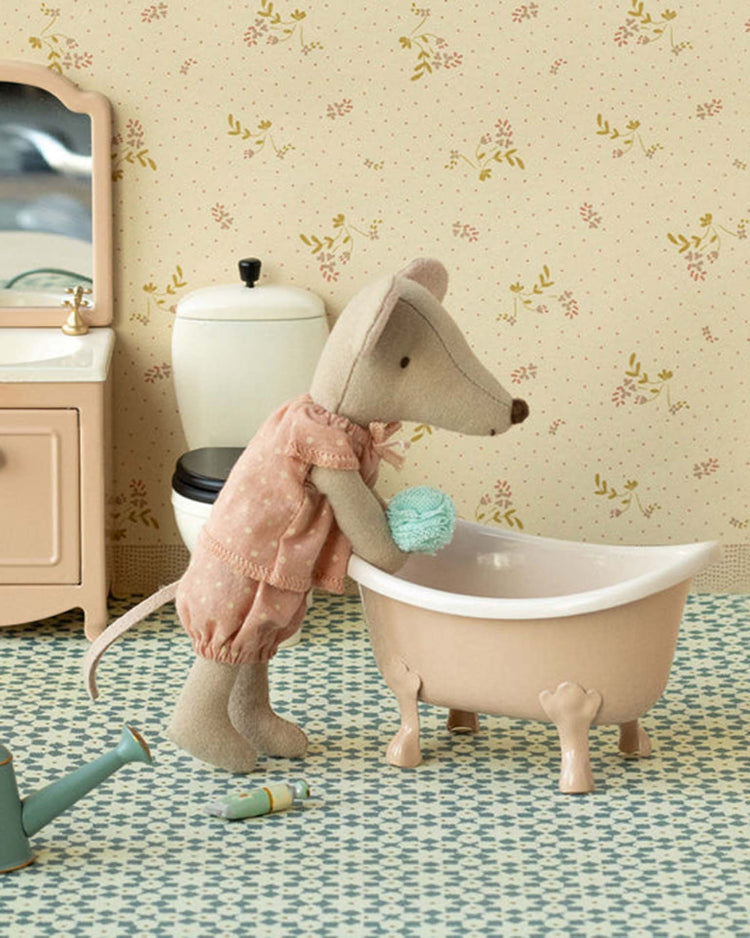 The "bathtub, mouse - rose" by maileg features a stuffed toy mouse in pink pajamas with a blue sponge, beside a vintage-style tub amidst charming mouse house furniture and floral wallpaper in a dollhouse bathroom.