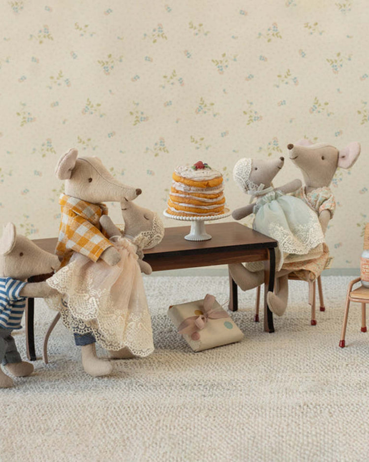 The maileg baby mouse in gown - mint joins three plush friends around a wooden table with a layered cake, creating a cozy, vintage-inspired tea party scene in soft pastels.
