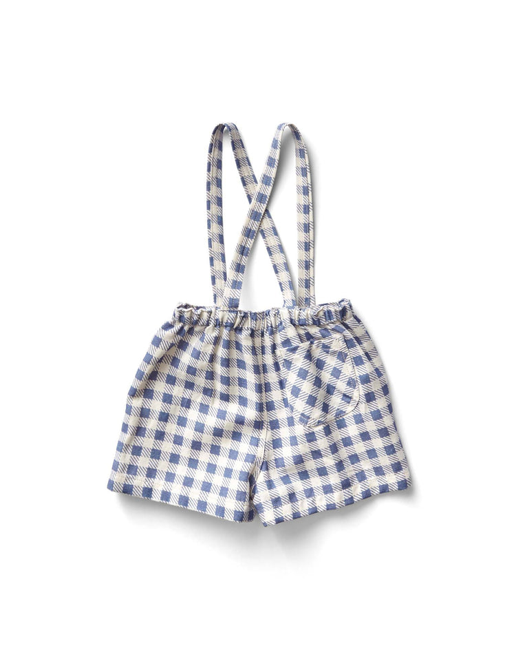 The enid shortall in gingham print, blueberry by soor ploom features charming blue and white checks with crossed suspenders. Made from soft cotton, these children's shorts rest elegantly against a crisp white background.