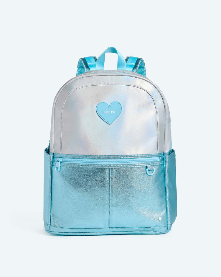 The State Bags Kane Large Double Pocket Backpack in Blue Iridescent features two side pockets, blue straps, and a heart-shaped patch on the front. Shown against a plain light background, it's the perfect stylish choice for school.