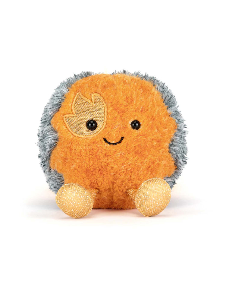 The Jellycat Amuseables Space Comet is a round, plush orange toy with fuzzy gray edges, gold glitter feet, a stitched smile, and an embroidered gold leaf over one eye—perfect for fans of space-themed cuddles.