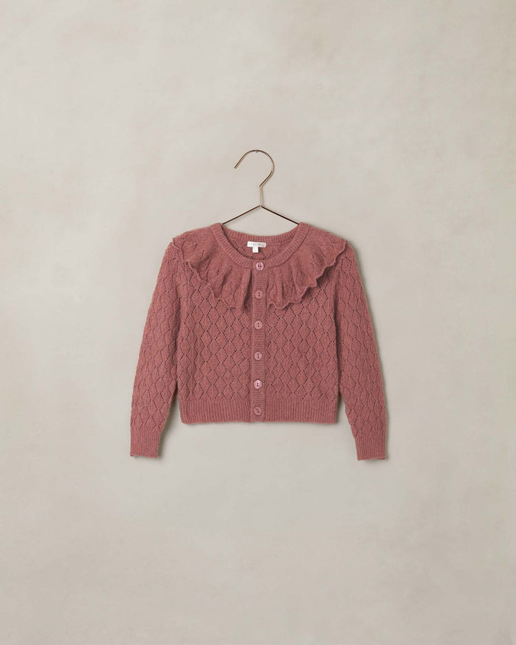 A spice-colored pointelle knit child’s ruffle cardigan sweater by noralee, featuring a ruffled collar, diamond pattern, and button front, is displayed on a hanger against a light beige background.