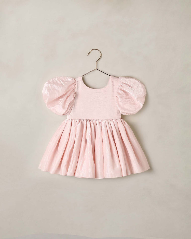 The sofia dress in rose shimmer by noralee features balloon puff sleeves, a fitted bodice, and a gathered skirt in pale pink, displayed on a simple hanger against a neutral background.