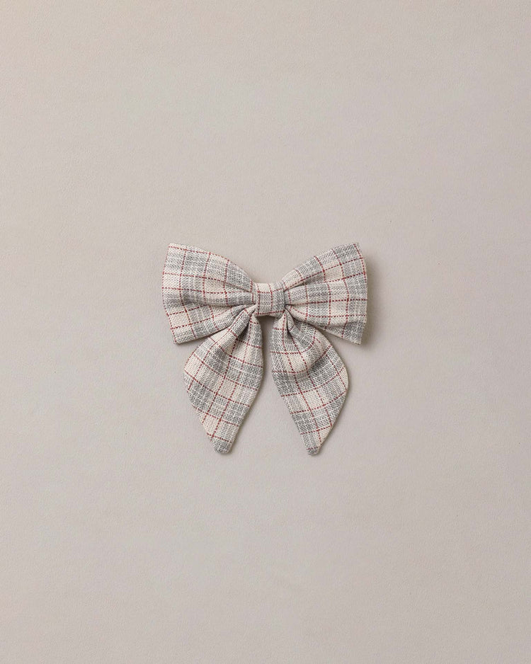 The norah bow in fall plaid by noralee features a gray fabric with a delicate red and white plaid design—an ideal fall accessory—displayed against a simple beige background. Crafted from viscose linen, this charming hair bow is finished with a rose gold alligator clip for secure and stylish wear.
