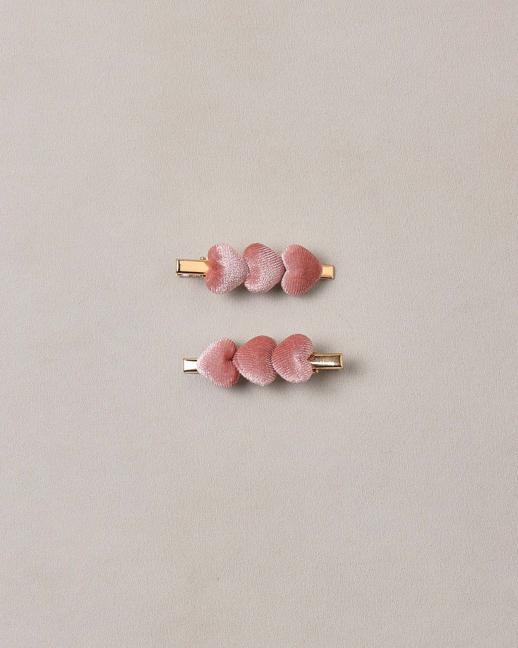 Two “velvet heart clips in spice” by noralee, each featuring rose gold alligator clip fastenings and adorned with three plush, pink velvet petals, are placed parallel to each other on a plain, light beige background.