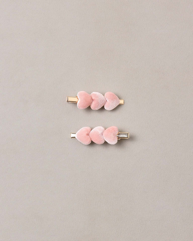 Two gold hair clips from noralee, each adorned with three soft pink plush velvet hearts, are displayed on a plain light gray background. The velvet heart clips in rose feature a stylish and secure rose gold alligator clip.