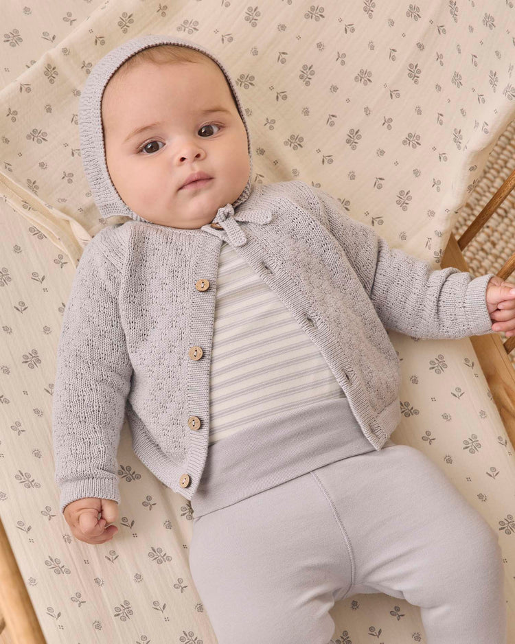 A baby lies on a patterned blanket, wearing the quincy mae side snap bodysuit + pant set in cloud stripe. The baby looks up with a calm expression.