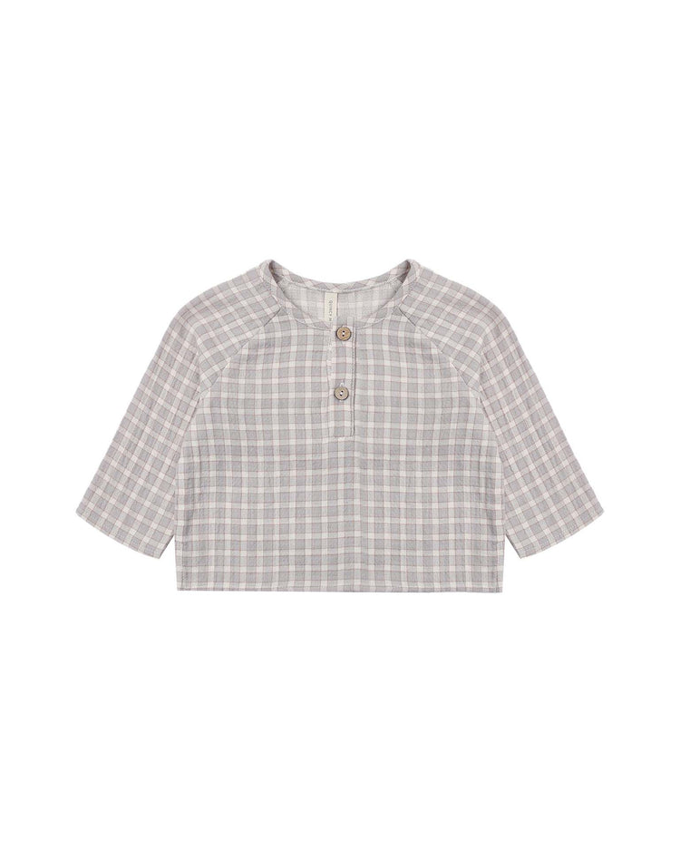 The zion shirt in blue gingham by quincy mae is a long-sleeve, relaxed fit children’s shirt featuring a round neckline and two brown buttons on the front placket, displayed laid flat on a white background.