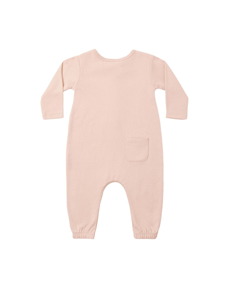 The long sleeve jumpsuit in dusty rose by quincy mae is a light pink, long-sleeve baby romper made from soft organic cotton. It features a single small pocket on the back right side and has elastic ankle cuffs. The jumpsuit is shown laid flat against a white background.
