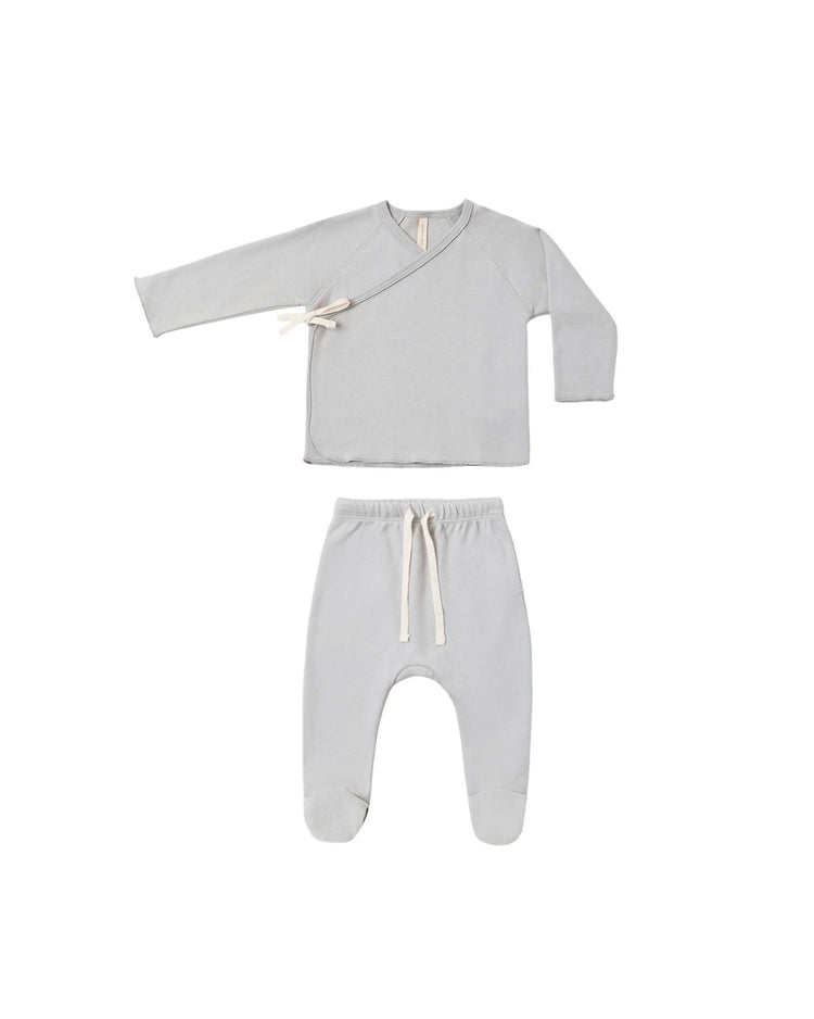 The wrap top + footed pant set in cloud by quincy mae is a light gray newborn coming home outfit made from organic cotton, featuring a long-sleeve baby wrap top with a side tie and matching footed pants with a drawstring waistband, displayed on a white background.