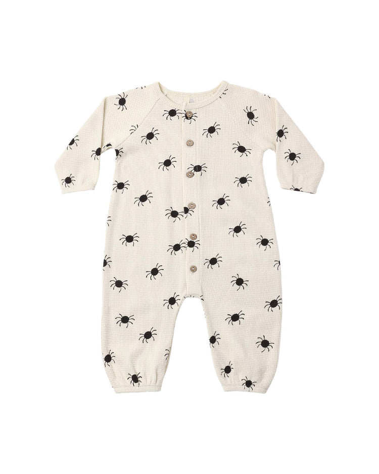 A waffle long sleeve jumpsuit in the bitsy spider print by Quincy Mae, featuring a cream color with black ant patterns and front buttons, made from organic cotton and laid flat on a white background.
