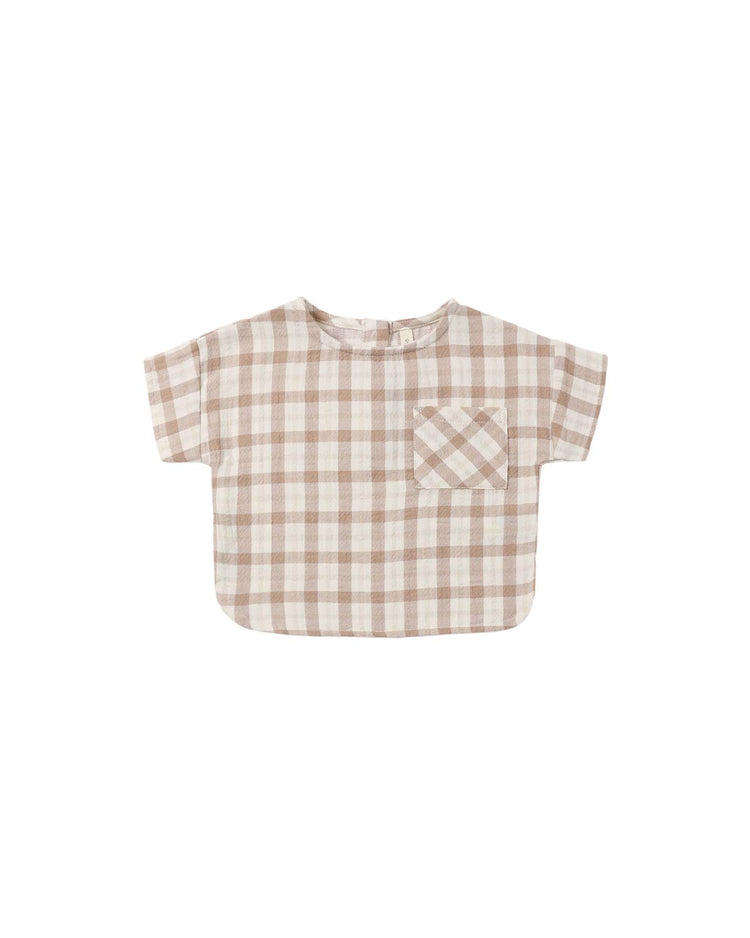 The "woven boxy top in rustic plaid" by quincy mae is a short-sleeve toddler shirt made from organic cotton, designed with a beige and white rustic plaid checkered pattern. It features a single front pocket on the left chest and has a relaxed, boxy fit, shown here laid flat on a white background.