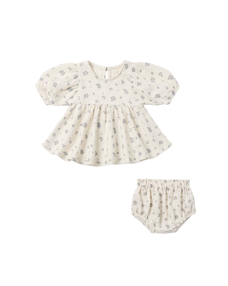 The francy set in winter berry by quincy mae features a cream-colored organic cotton dress with puffed sleeves and a gathered waist reminiscent of an empire waist top, paired with matching bloomers. Both pieces are adorned with a delicate small floral print and the dress has a slightly flared skirt. The set is displayed against a white background.