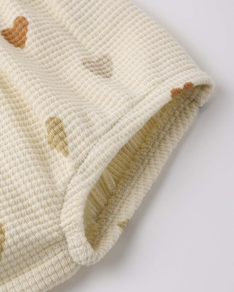Close-up of cream-colored organic cotton waffle knit fabric with brown and beige heart shapes, highlighting the finished edge of the quincy mae darla dress in confetti hearts.
