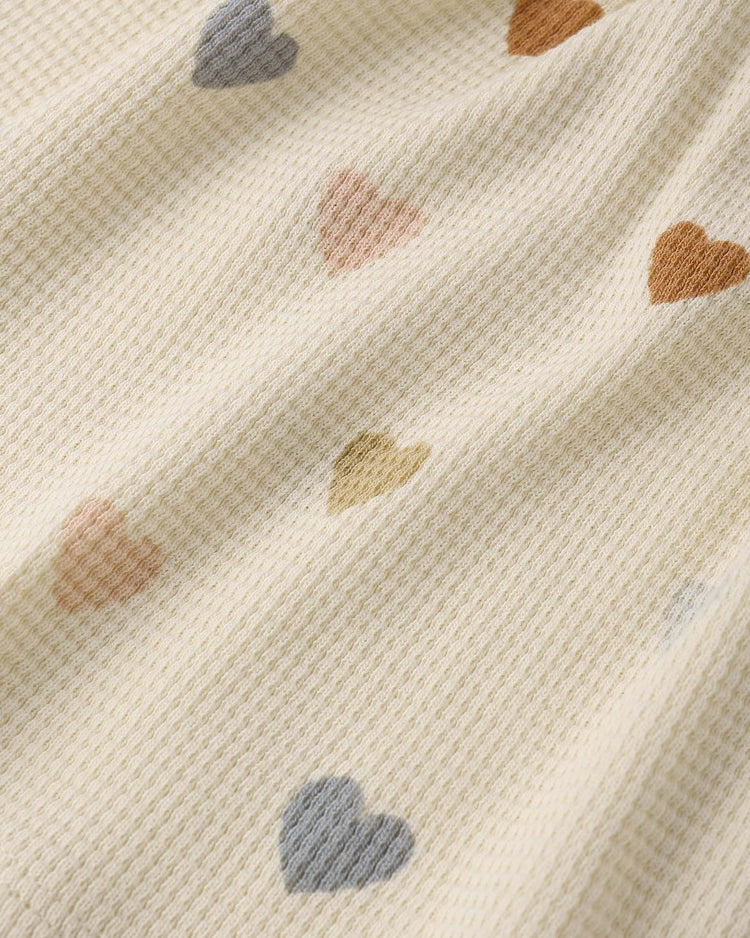 A close-up of the darla dress in confetti hearts by quincy mae, featuring textured cream organic cotton adorned with small pastel heart shapes in blue, pink, yellow, and brown.