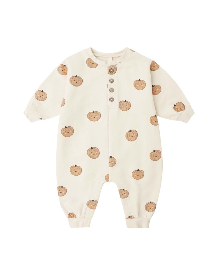 The relaxed fleece jumpsuit in pumpkins by quincy mae is a cream-colored baby romper with long sleeves and an adorable brown pumpkin print. Made from organic cotton, it features four buttons down the chest, elastic cuffs at the wrists and ankles, and a plain white background.