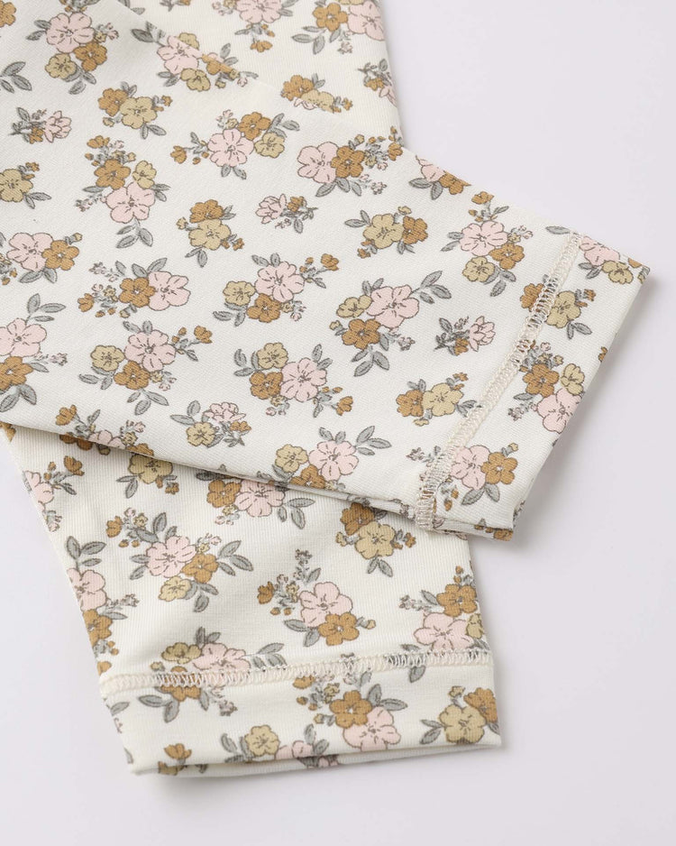 Close-up of quincy mae's bamboo short sleeve pajama set in wildflower, featuring cream-colored soft bamboo fabric with small pink, yellow, and brown flowers and green leaves, plus detailed stitching on overlapping sleeves—perfect for cozy baby pajamas.