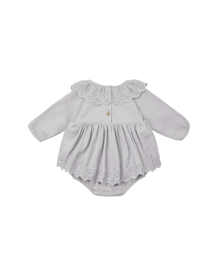 The thalia romper in cloud by quincy mae is a light gray organic cotton baby romper featuring long sleeves, a ruffled collar, and delicate eyelet lace trim on the skirt and collar. This charming piece has a back button closure and is displayed on a white background.