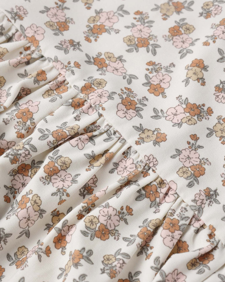 A close-up shows the quincy mae bamboo babydoll dress in wildflower, made of soft bamboo with a pink, orange, and tan floral print and grey-green leaves. The dress features ruffle sleeves for a delicate finish.